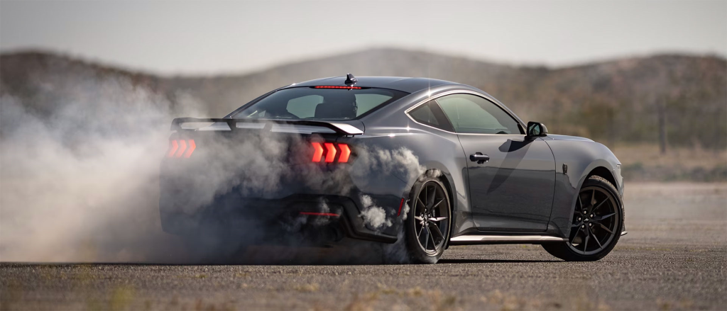 A sporty gray Ford Mustang drifting with smoke billowing from the rear tires.