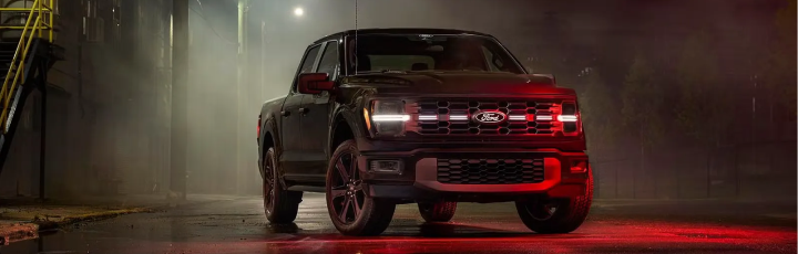 Black Ford F-150 with its LED light bar lit, parked in a dark, misty industrial lot
