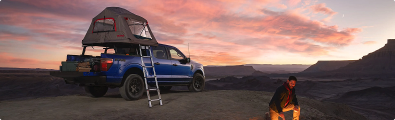 Blue Ford F-150 with a rooftop tent on the bed, parked in the desert at sunset
