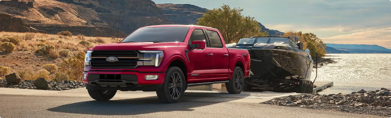 Red Ford F-150 towing a boat along a waterfront road
