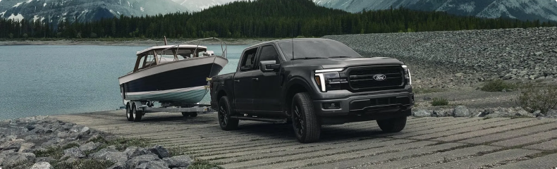 Dark gray Ford F-150 towing a boat up a lakeside boat ramp