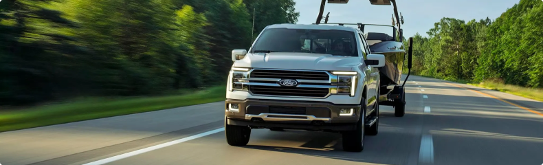 Silver Ford F-150 towing a boat on a tree-lined highway