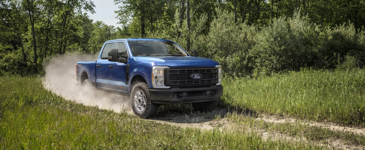 Blue Ford Super Duty Crew Cab kicking up dust on a grassy dirt trail