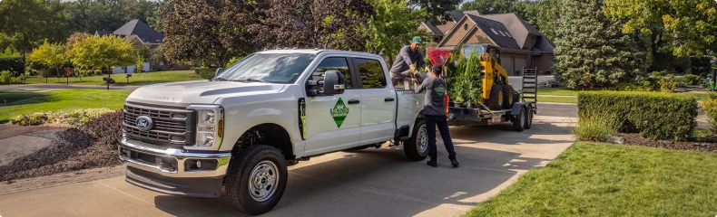Landscaping crew unloading plants from a white Ford Super Duty work truck and trailer