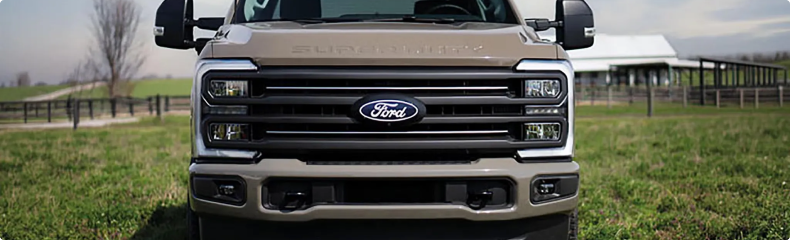 Front view of a tan Ford Super Duty grille on a farm with fenced pasture