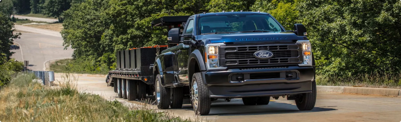 Dark blue Ford Super Duty towing a flatbed gooseneck trailer on a curving road