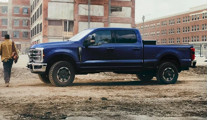 Blue Ford Super Duty Crew Cab parked on a dirt lot beside brick buildings