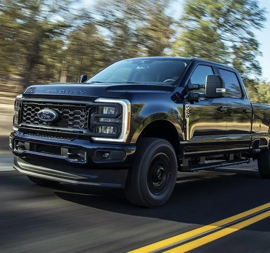 Black Ford Super Duty Crew Cab driving on a two-lane road through the trees
